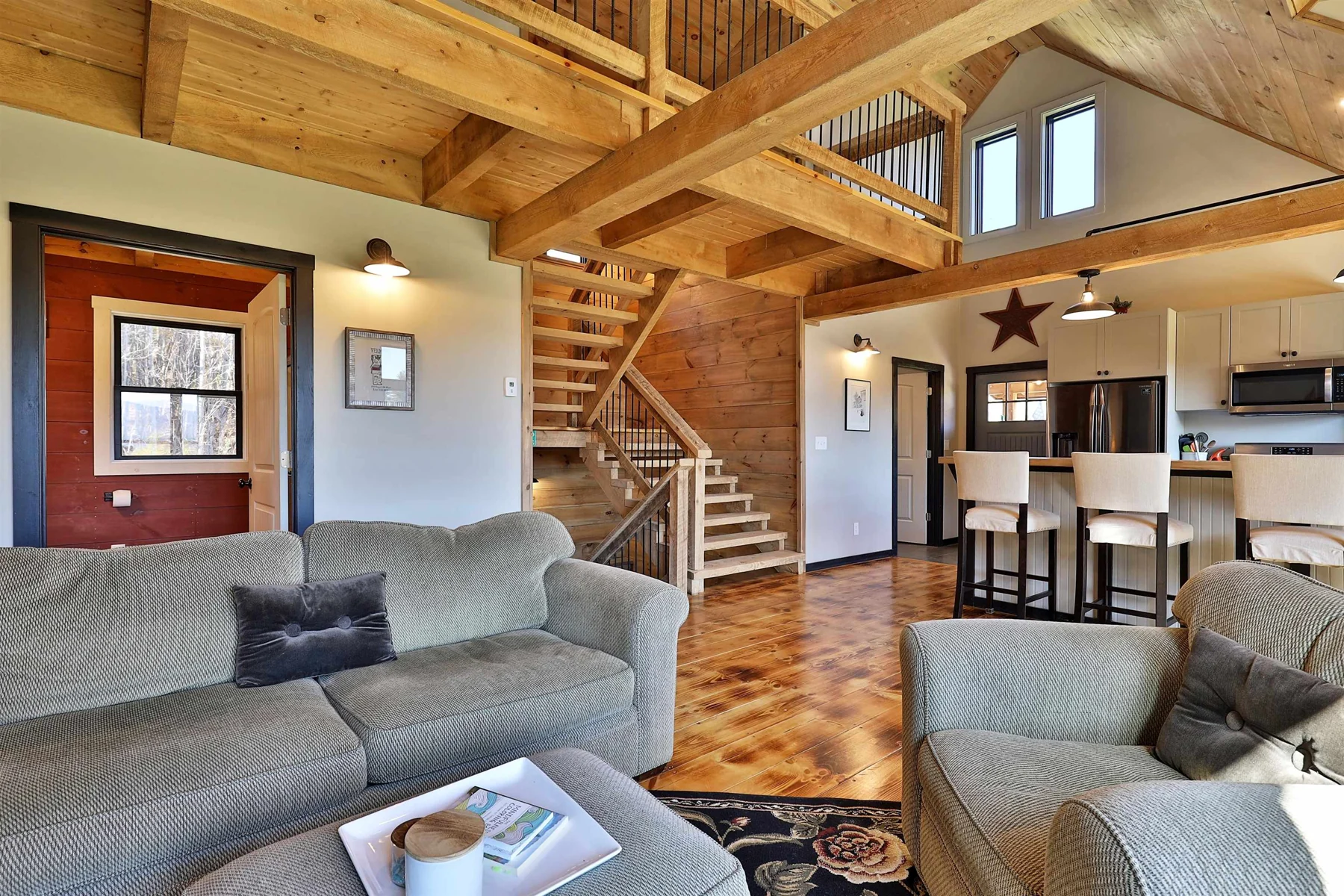 A sitting area opens to the kitchen and wood staircase beneath exposed timbers.