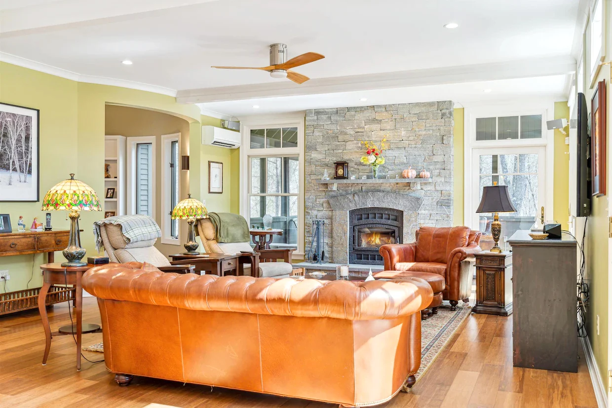Living room with a stone fireplace, wood floors and an orange leather sofa in a Hudson Design and Build renovation on Westerdale Road, Woodstock, Vermont.