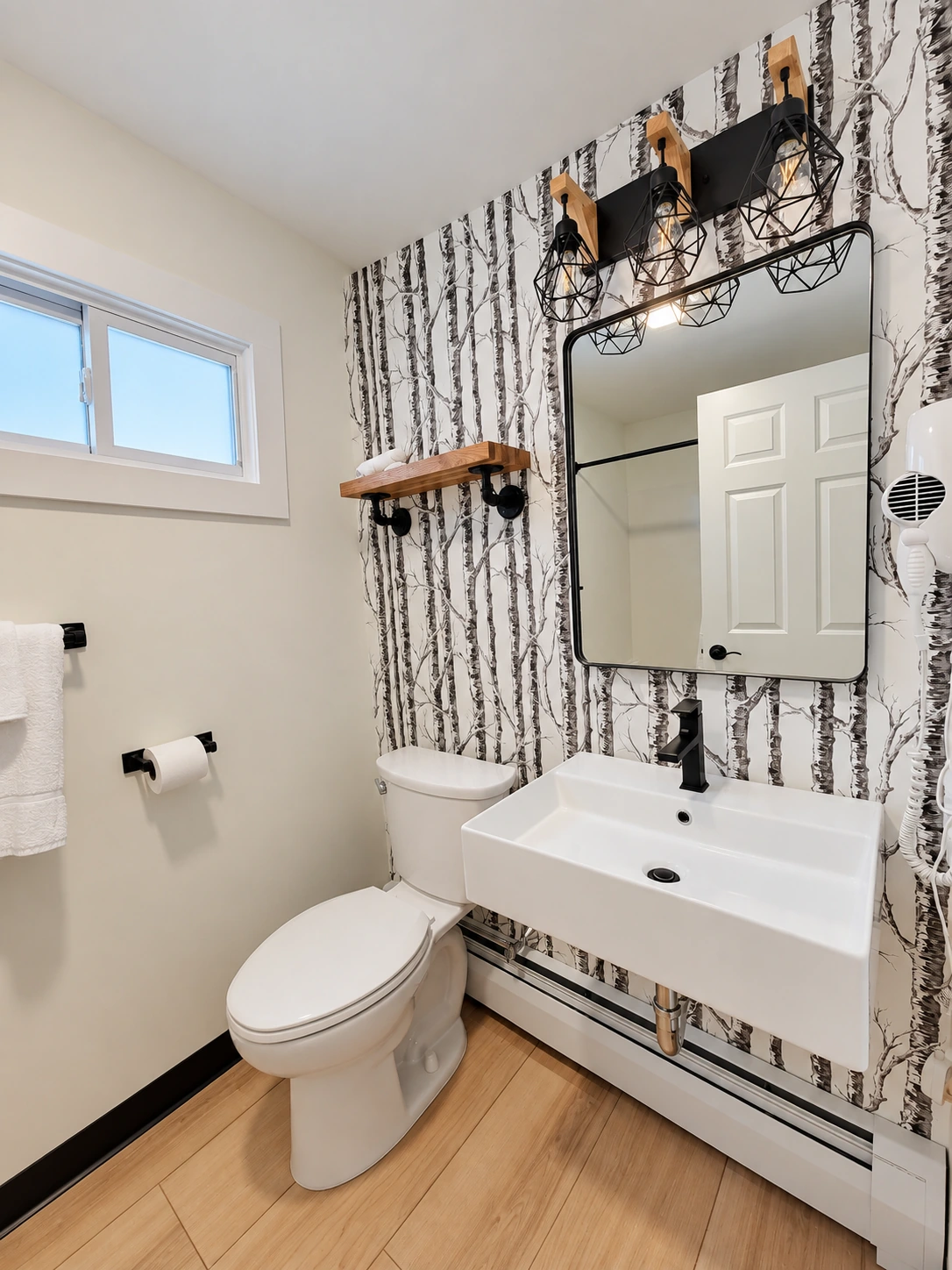 Birch-pattern wallpaper, a white pedestal basin and wood shelving in a powder room.