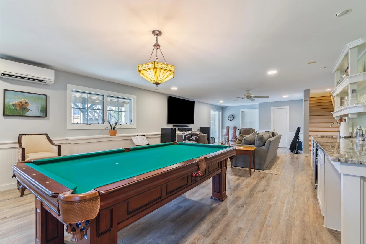 A pool table in a finished lower-level room, with built-in cabinets and a sitting area beyond.