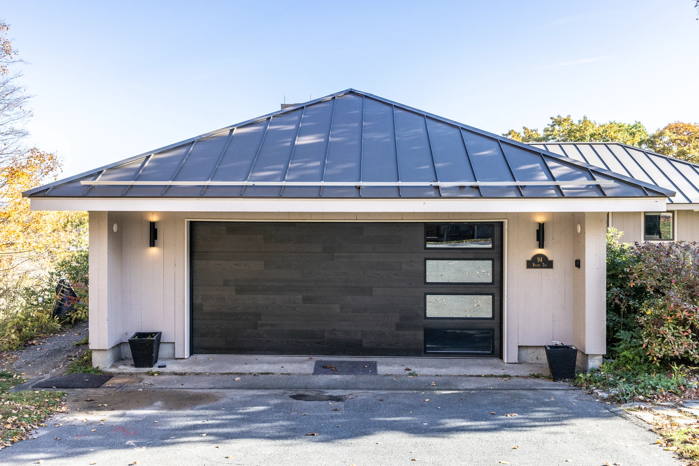 Quechee home garage with a standing-seam roof, wood-look door and illuminated exterior sconces.