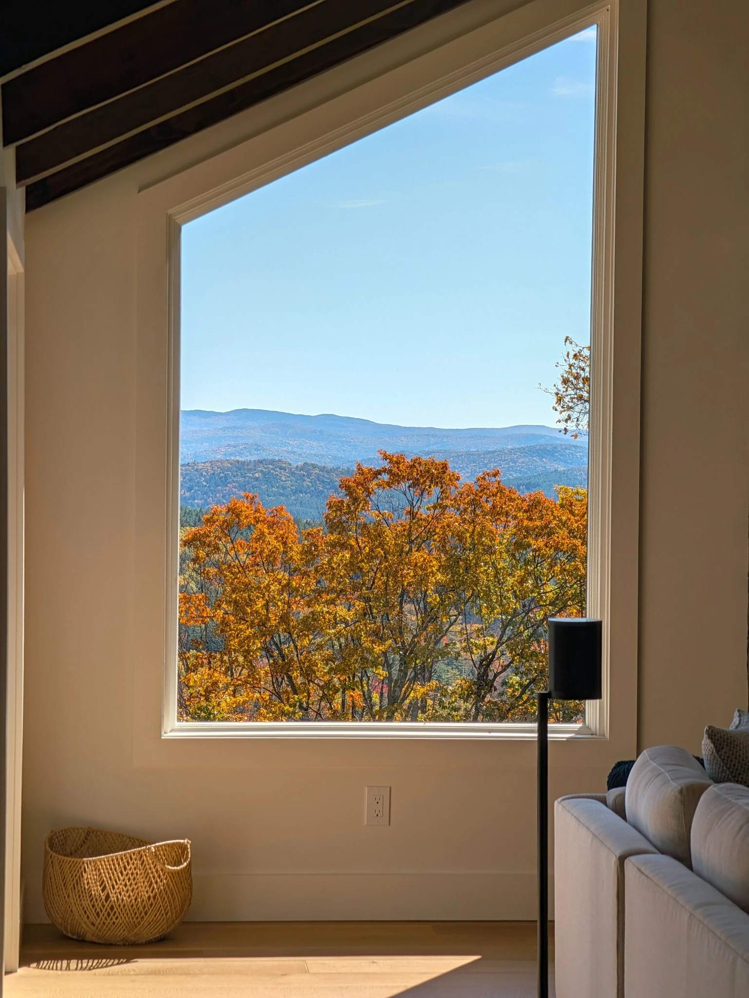 Autumn foliage and distant mountain ridges framed by a tall window beside a sofa.