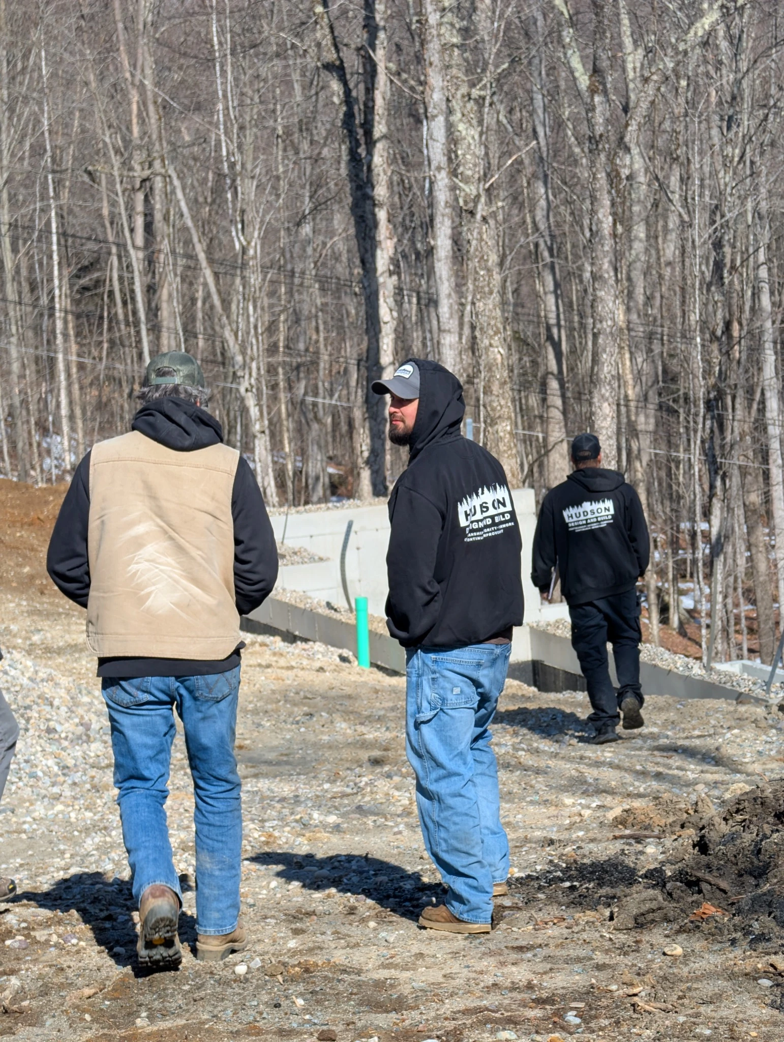 Three Hudson crew members walking a wooded construction site in branded workwear.