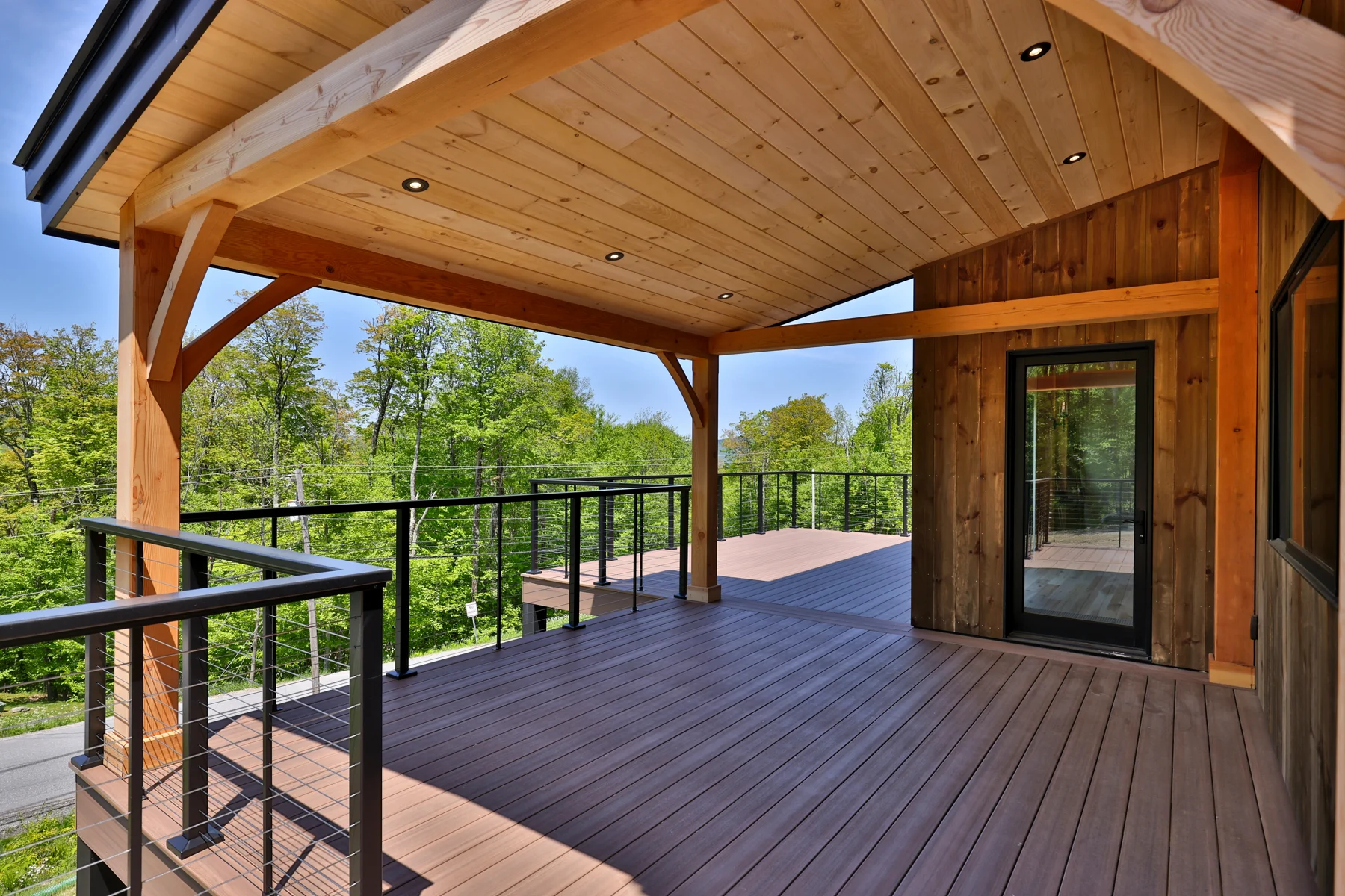 Covered deck with exposed timber framing and dark railings on a Hudson Design and Build custom home in Killington, Vermont.