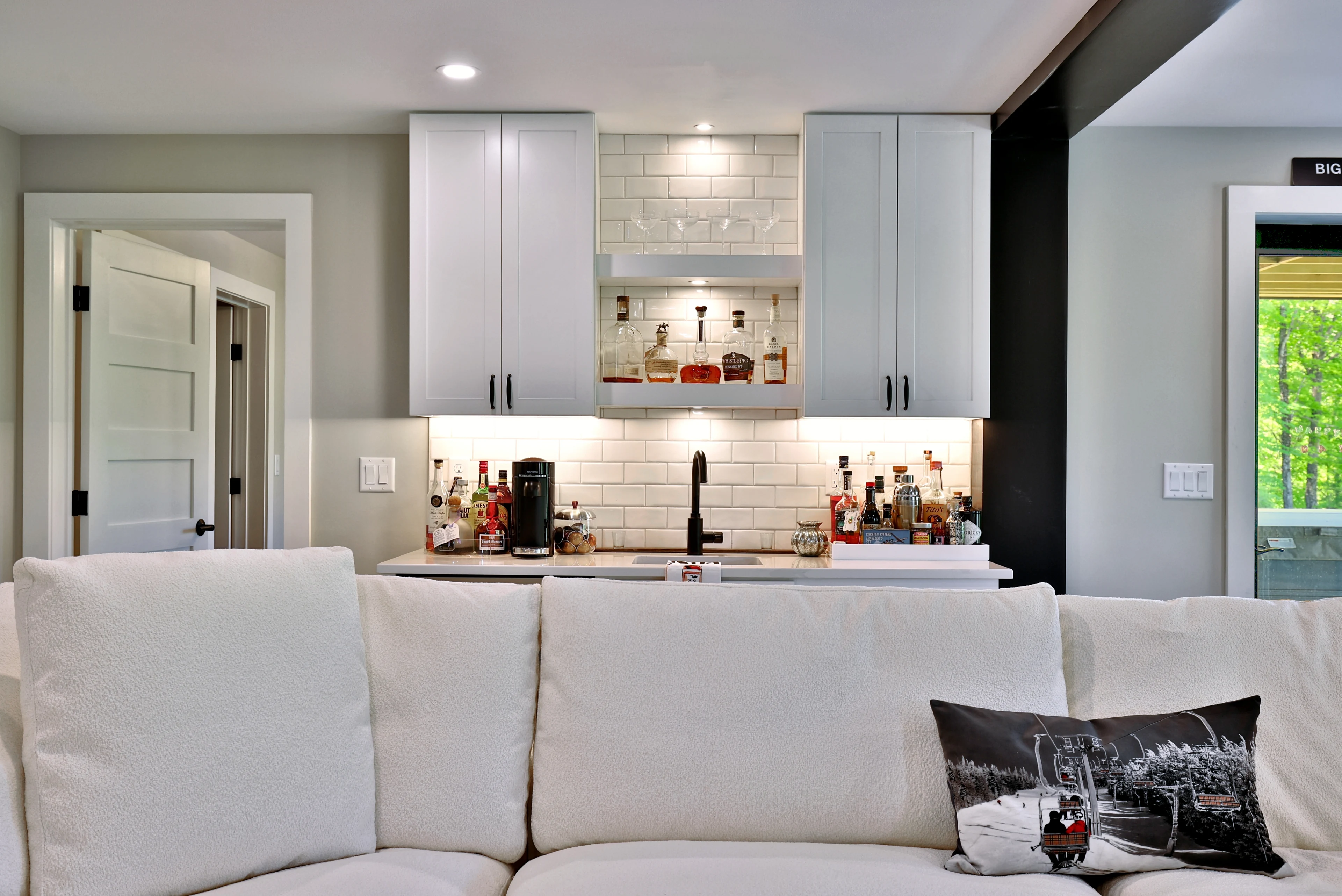 White bar cabinetry, a tile backsplash and a black faucet behind a seating area in a Killington home.