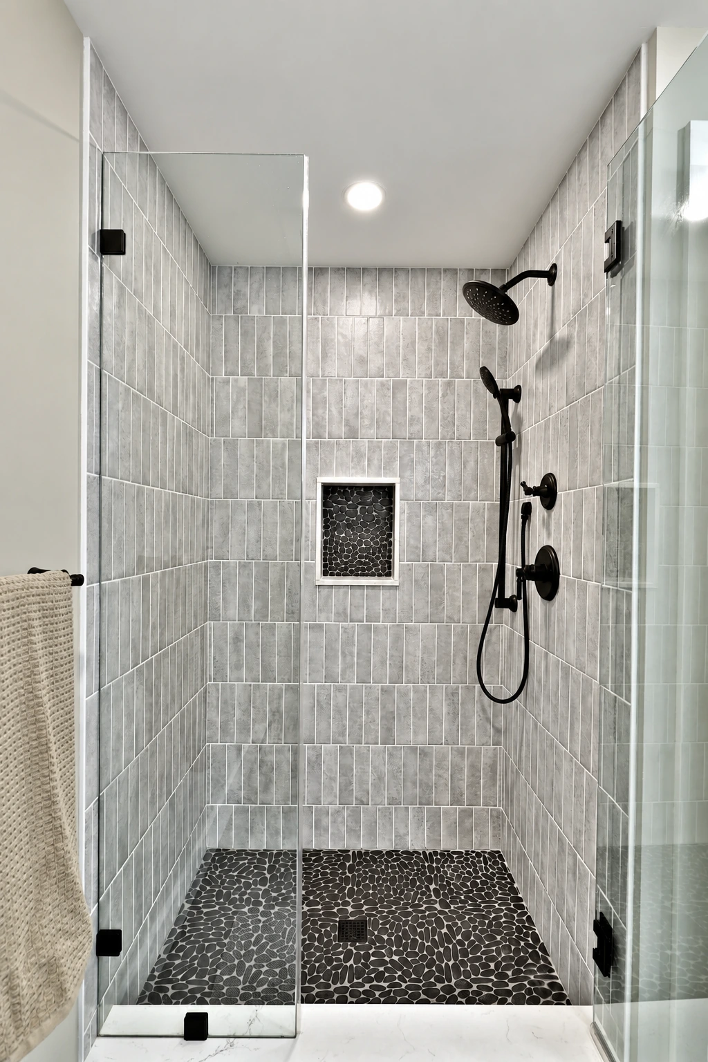 Slim vertical shower tiles, a recessed niche and black shower fittings.