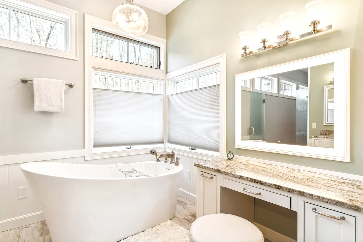 A freestanding white bathtub beneath windows beside a long vanity and mirror.