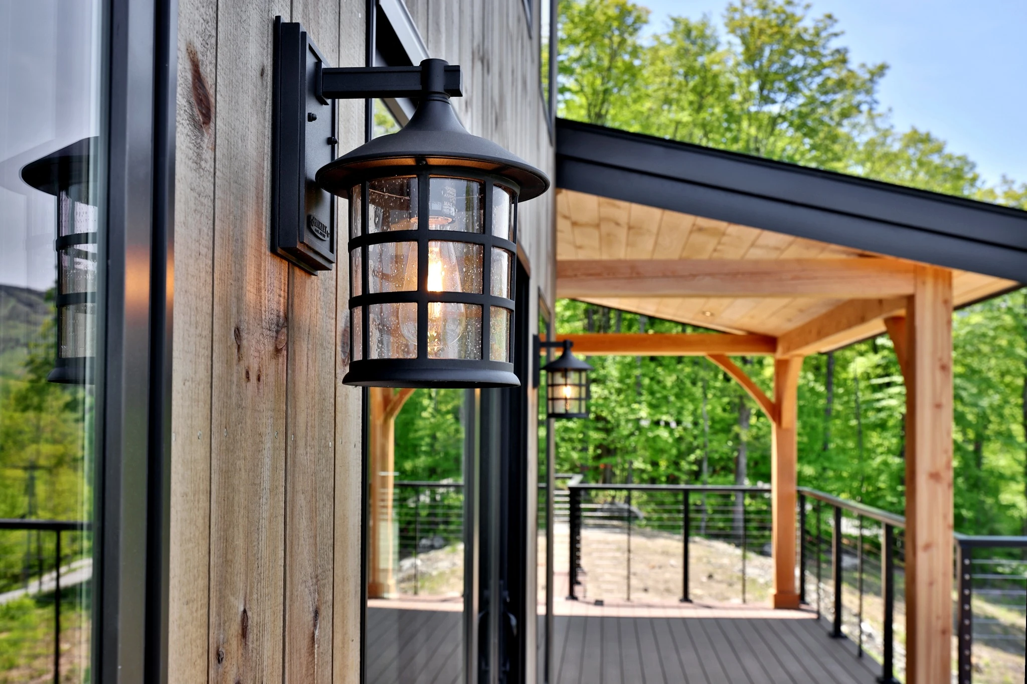 Black metal wall lantern beside wood siding and a covered timber deck.