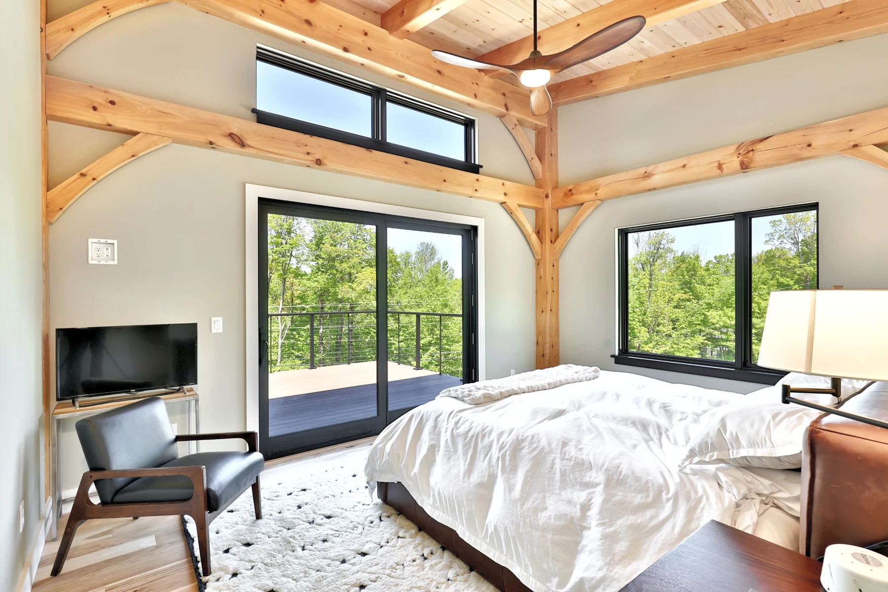 Bedroom with exposed timber beams and large woodland-facing windows in a Hudson Design and Build custom home in Killington, Vermont.
