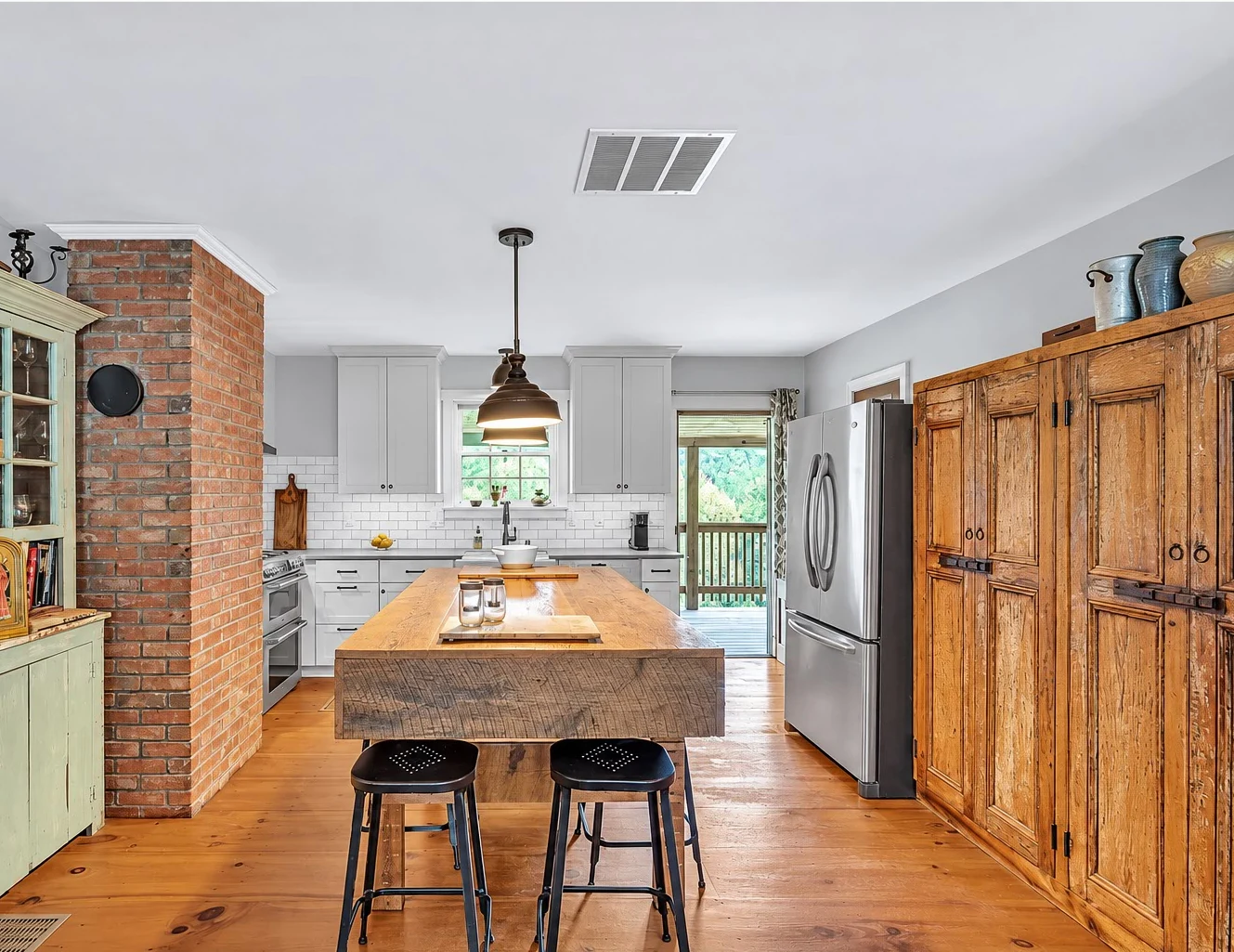 Kitchen with an exposed brick chimney, wood island, warm wood floors and gray cabinetry.
