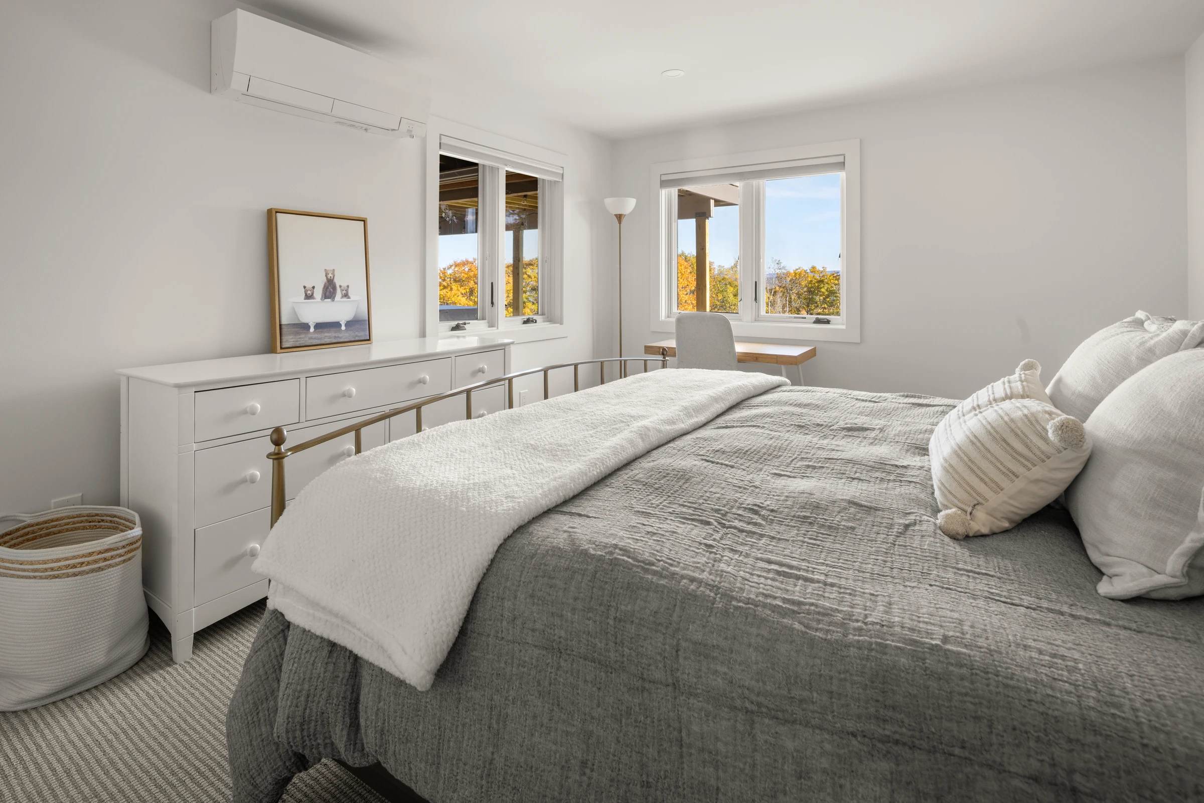 Bright bedroom with pale cabinetry, textured bedding and windows overlooking autumn foliage.
