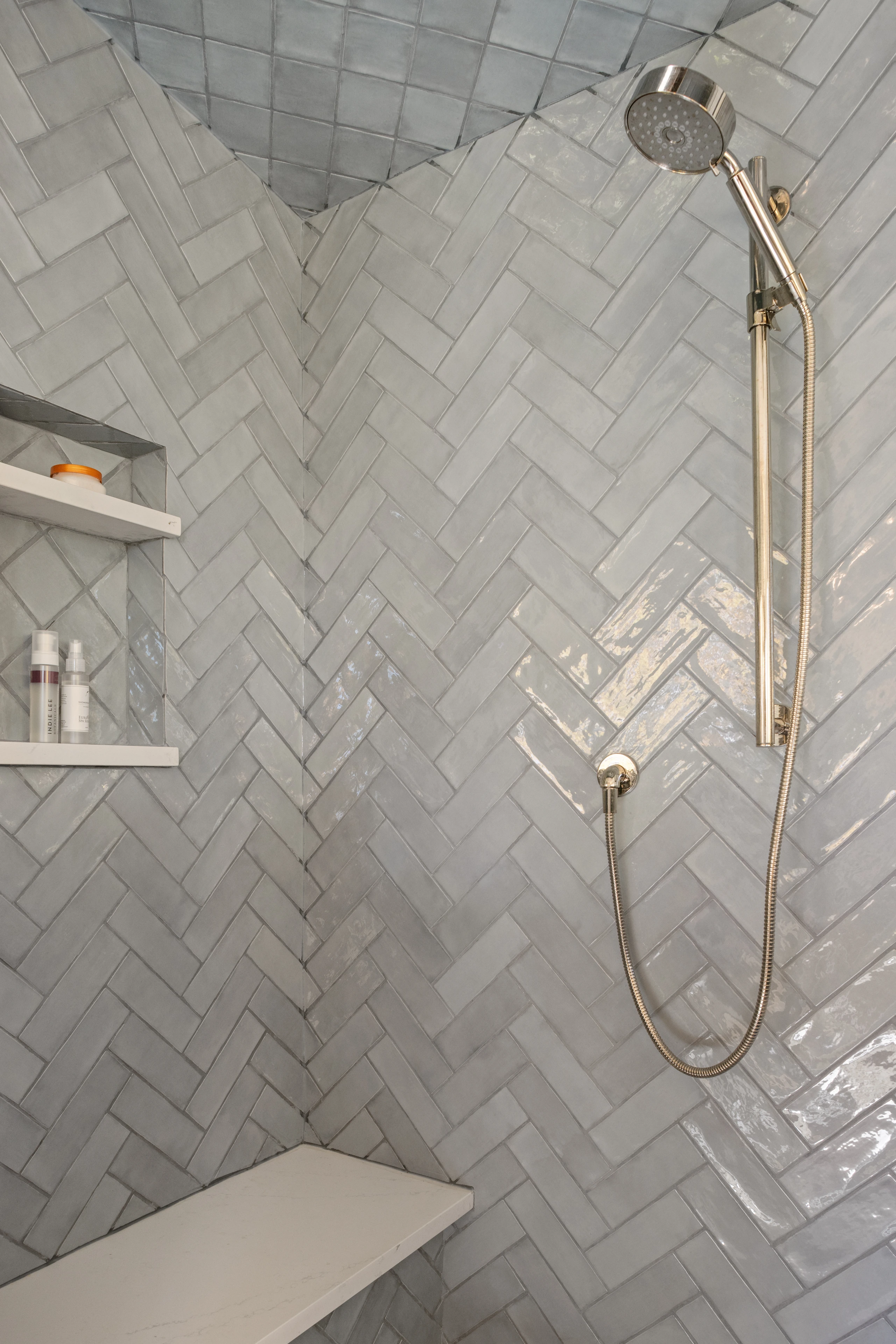 Bathroom shower with herringbone tile, a built-in bench and brass-tone fixtures in Quechee.