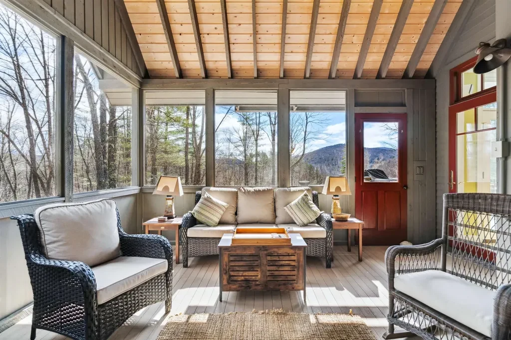 Screened porch with a timber ceiling, lounge seating and woodland views at Woodstock, Vermont.