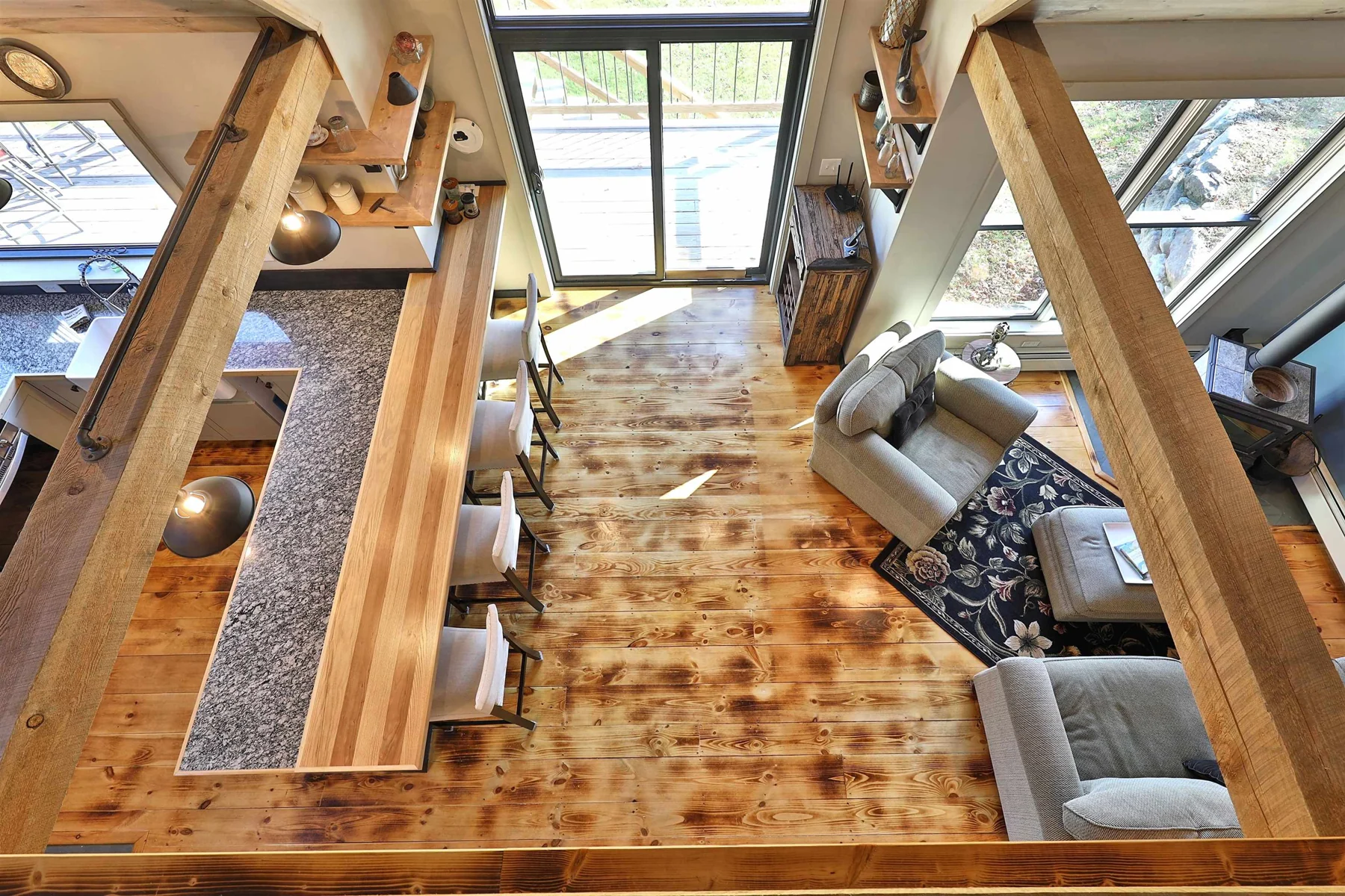 An overhead view from the mezzanine of the wood floor, seating area, timber frame, and tall windows.