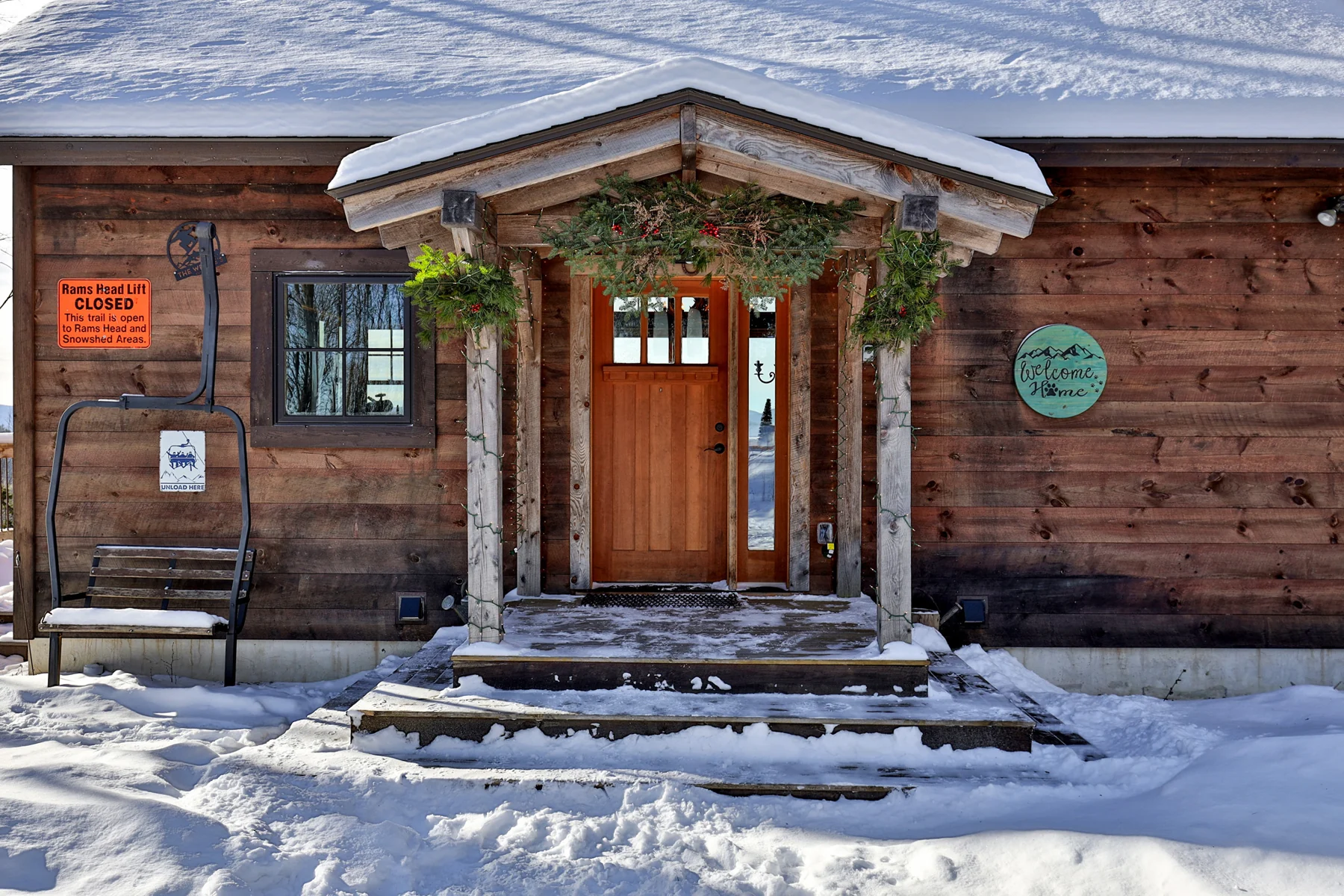 A wood front door beneath a timber porch with stone steps and snow.