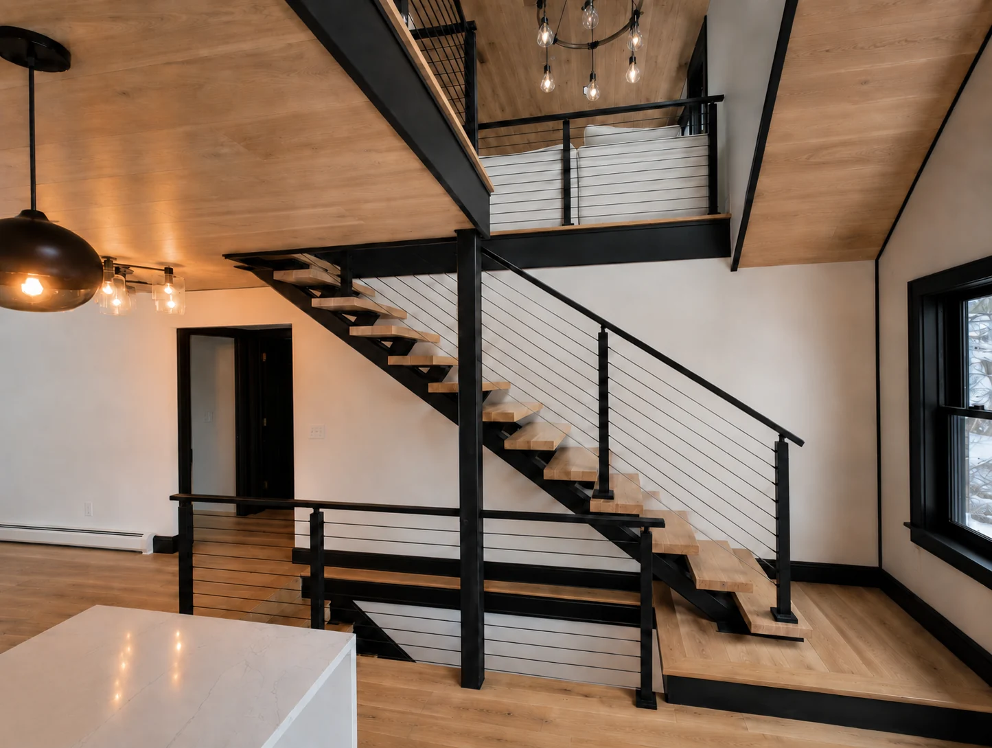 Open wood staircase and black railing connecting the kitchen level to a mezzanine beneath a wood ceiling.