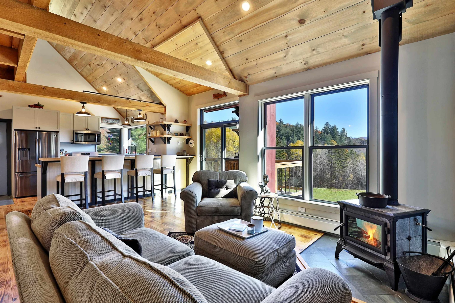 Open living room with a wood stove, timber ceiling and broad windows in a Hudson Design and Build home in Stockbridge, Vermont.