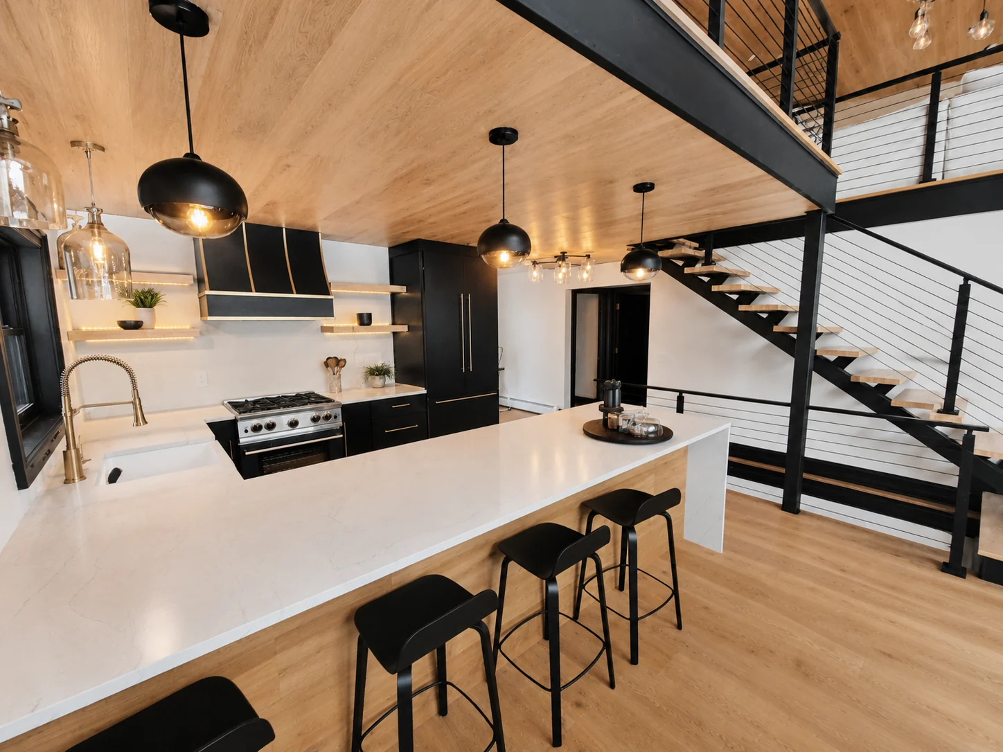 Black cabinetry, a white island with stools, and an open wood stair beneath a wood ceiling.