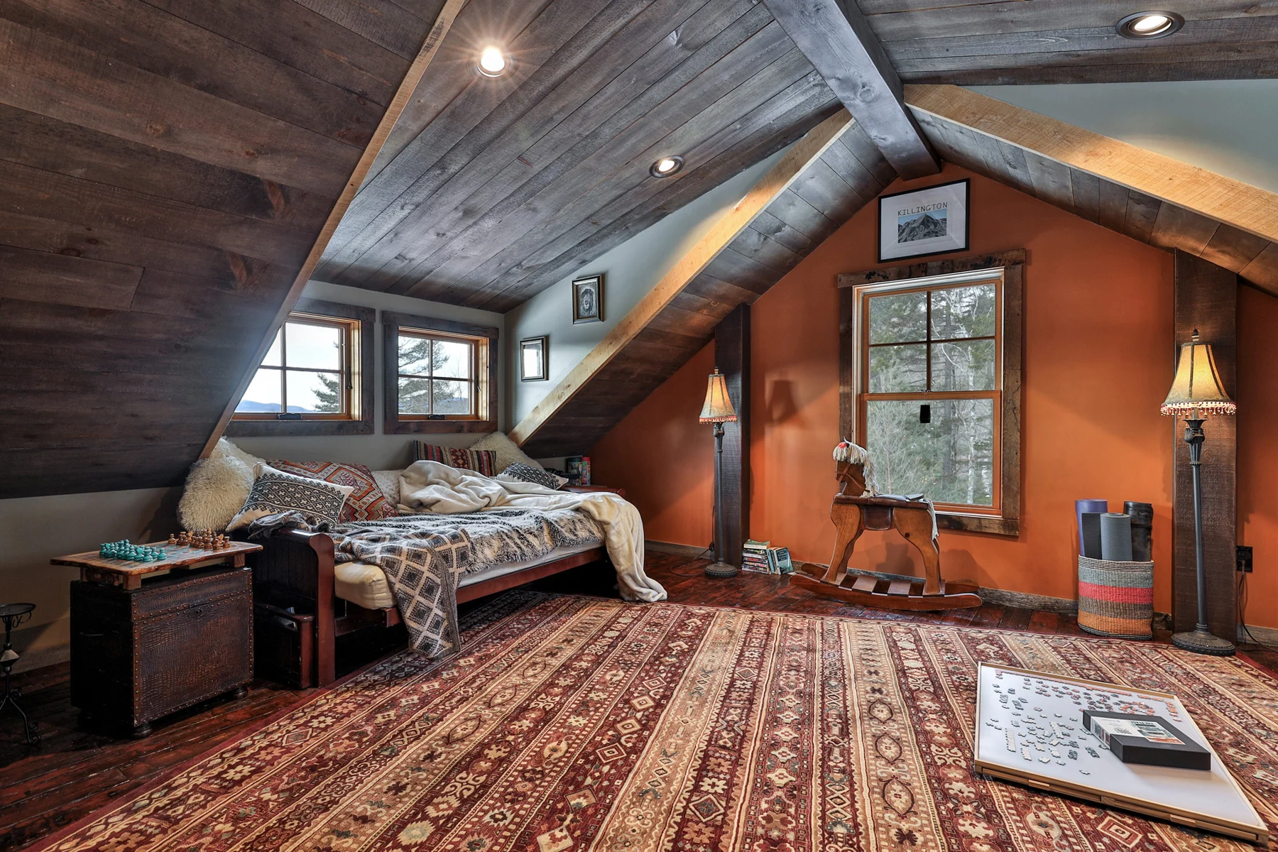 Bedroom beneath a sloping timber ceiling with mountain-facing windows in a Hudson Design and Build ski home near Killington, Vermont.