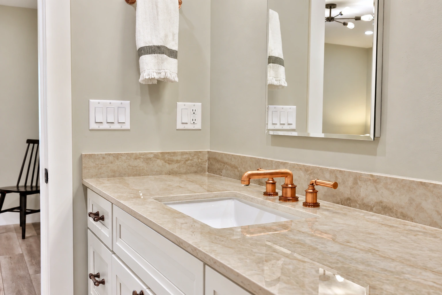 Pale stone vanity top with a copper-toned faucet and white cabinetry.