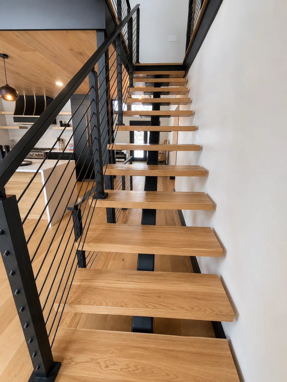 Open wood stair treads with black metal railing against a white wall.