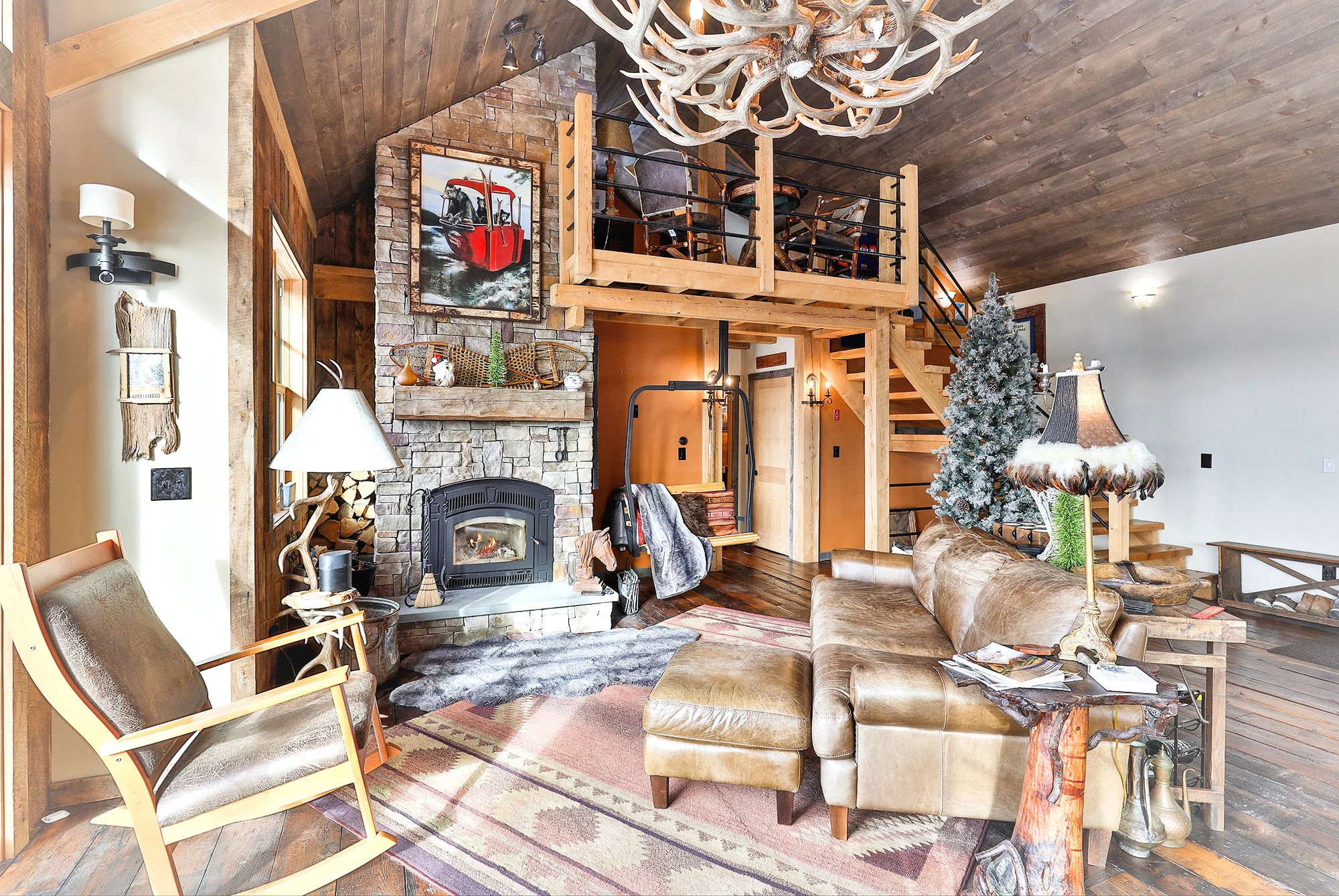 Timber-framed gathering room with a tall stone fireplace and mountain-facing windows in a Hudson Design and Build ski home near Killington, Vermont.