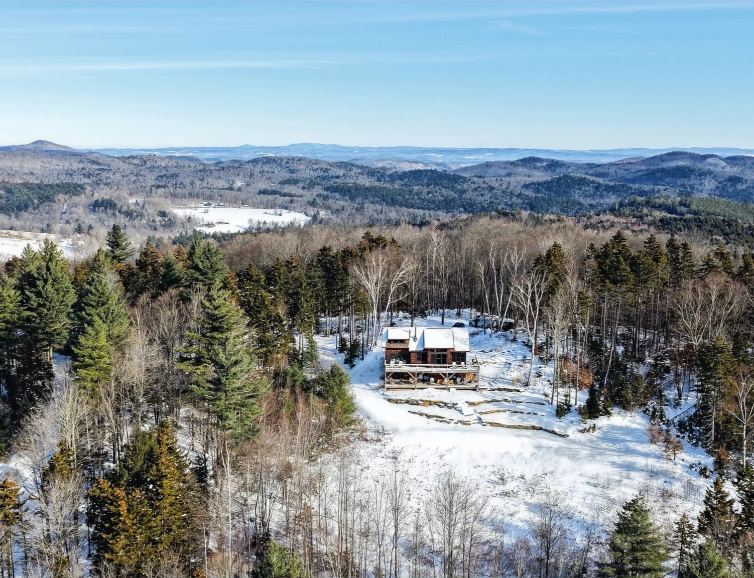 A timber home surrounded by snowy trees, with a broad mountain ridgeline beyond.
