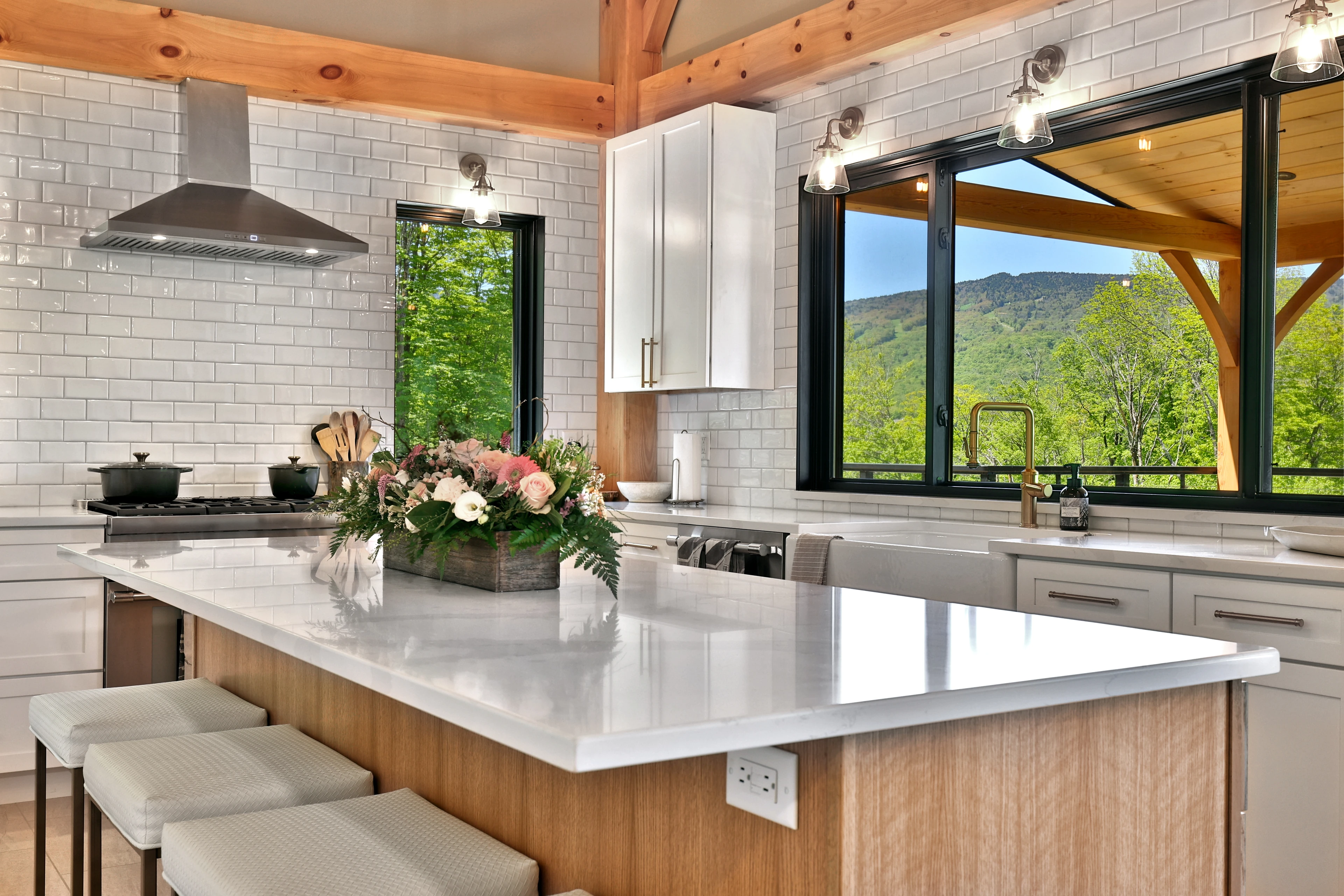 Custom kitchen with a wood island, pale counters and mountain views in a Hudson Design and Build timber frame home in Killington, Vermont.