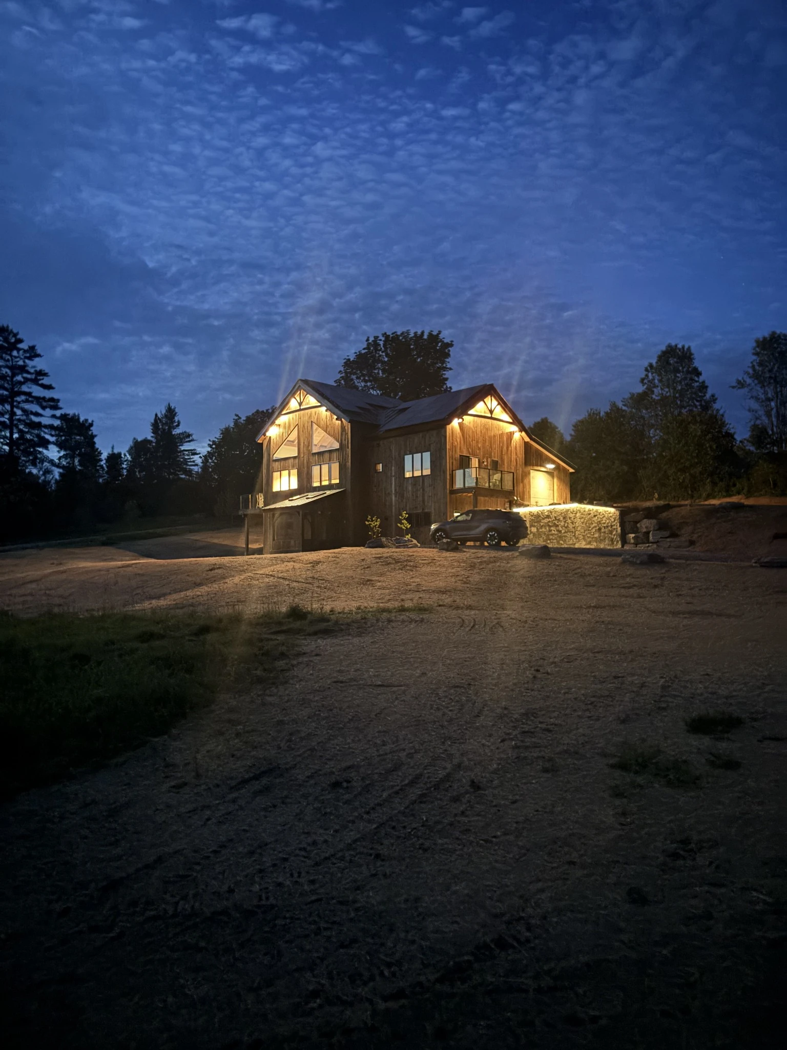Warm windows and exterior lights on a timber home beneath a deep blue evening sky.
