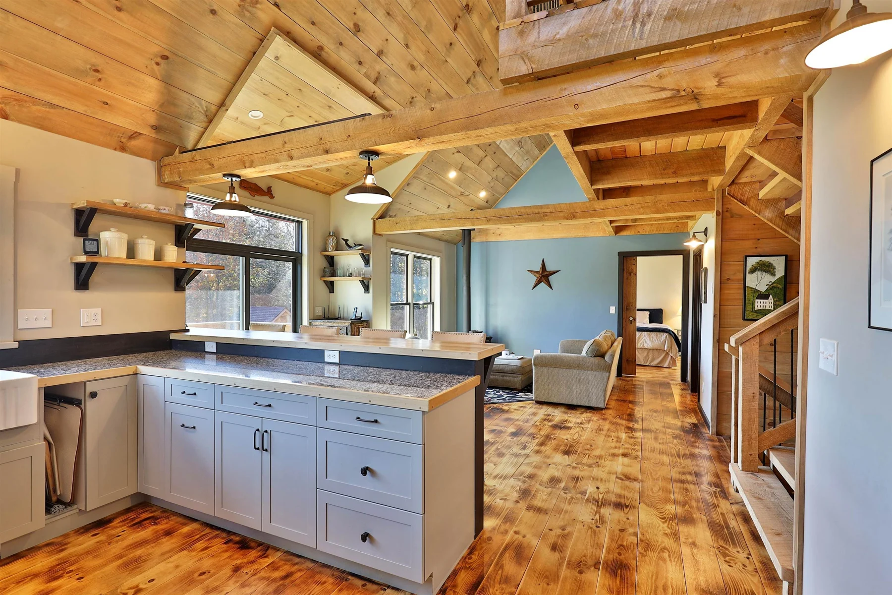 Open kitchen with a gray island, wood floors and exposed beams in a Hudson Design and Build timber frame home in Stockbridge, Vermont.