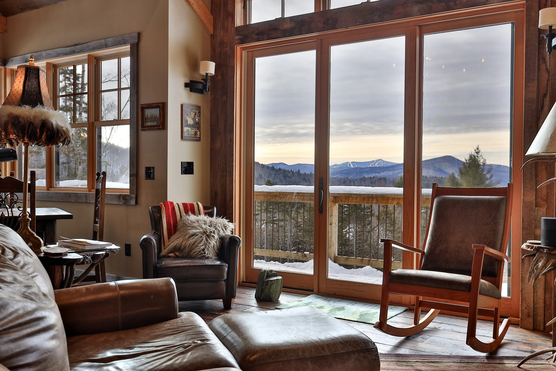 Chairs and a sofa face tall windows and doors with a distant mountain view.