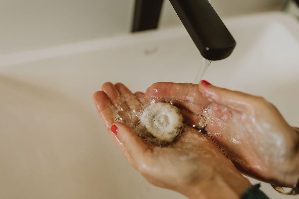a hand is holding a small size shampoo bar under a black tap the shampoo bar is lathered and has foam on it