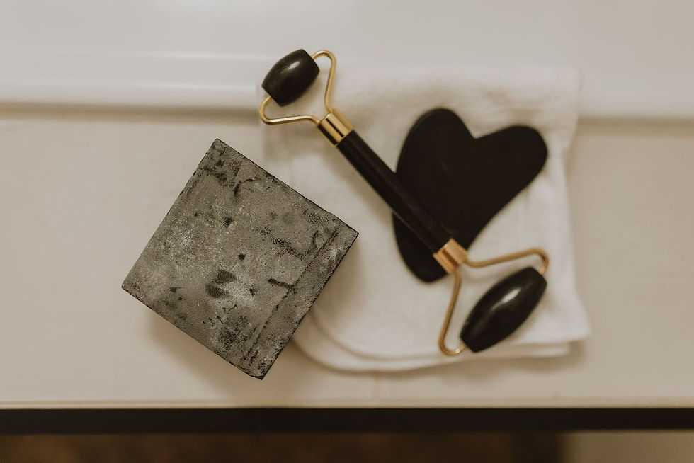 A bar of black soap sits on the edge of a white bath, beside the soap is a black jade gua sha face tool and roller