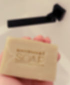 a single rectangular bar of light green soap is being held in front of a black tap wear soap is stamped handmade soap