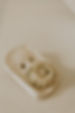 a white ceramic soap dish in a rectangle shape looks handmade with a small flower shaped bar sitting on top the background is a white marble bathroom benchtop