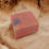 Thumbnail: A single rectangular bar of soft pink soap with blue and yellow mica speckled on the top sits on a wooden, earthy  backdrop