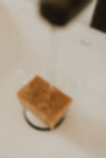 one bar of soap in a bath under a tap with running water shown hitting the soap water droplets splashing soap is honey colour