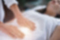 Female therapist performing Reiki therapy treatment holding hands over woman's stomach. Al