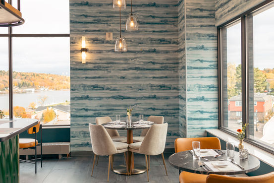 A panoramic view of the Observatory Lounge’s cozy interior, featuring rich wood tones, Lake Superior-inspired blues, warm sandstone accents, bold colors, and atmospheric lighting. Located in Downtown Houghton with views of Hancock, Michigan and the Quincy Smelter, Keweenaw National Historic Park.