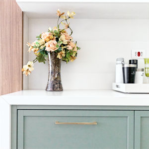 Armários de cozinha em tom verde sálvia com puxadores dourados e bancada branca em apartamento de luxo. Design de interiores 