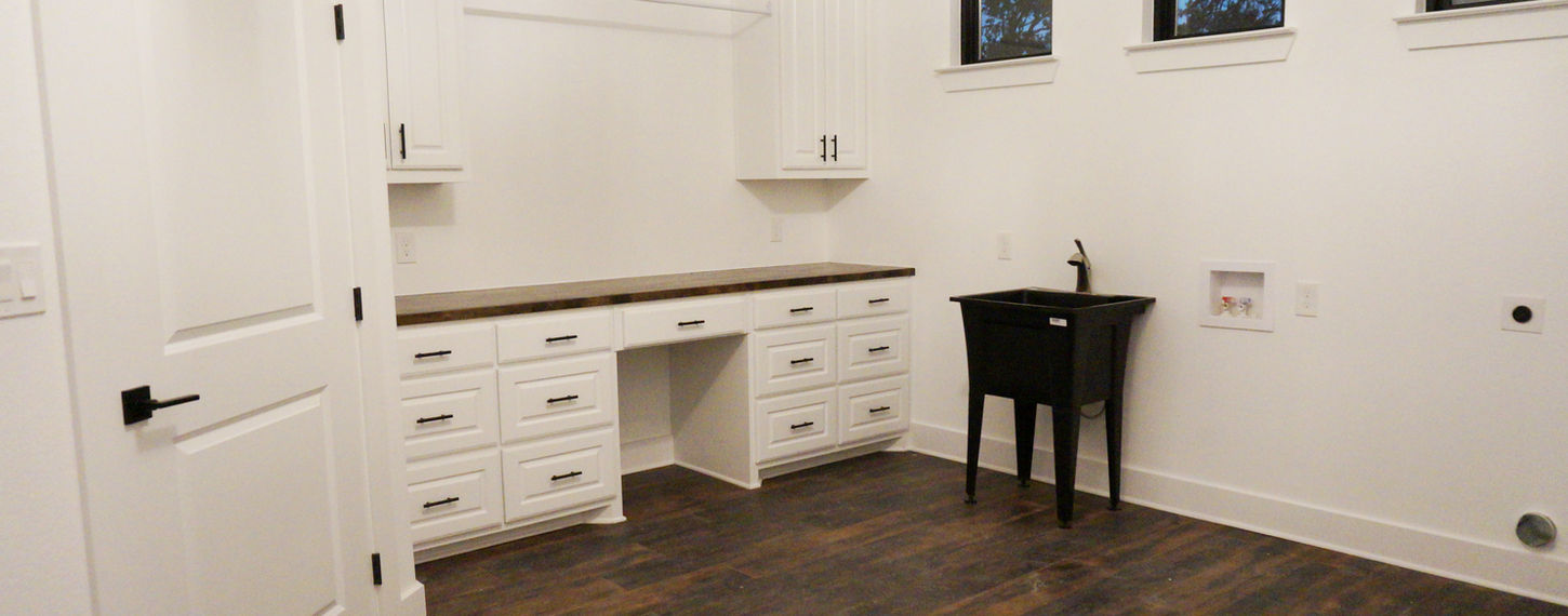 Remodeled laundry room with white cabinets, a black utility sink, wooden flooring, and three small windows near the ceiling.