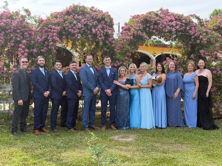 wedding party posing for photo in front of arched rose garden