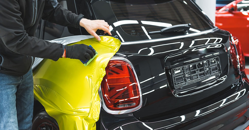 Someone places a bright yellow vinyl on the side of a black car. They are using a tool to smooth the wrap over the vehicle.