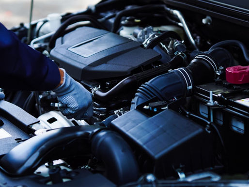 A close-up of an open hood of a car to reveal the engine. A person wearing gloves uses a wrench to tighten a component.