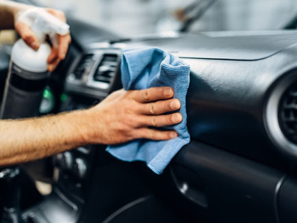 A person is cleaning the dashboard of a car, they are using a cloth and have a spray bottle.