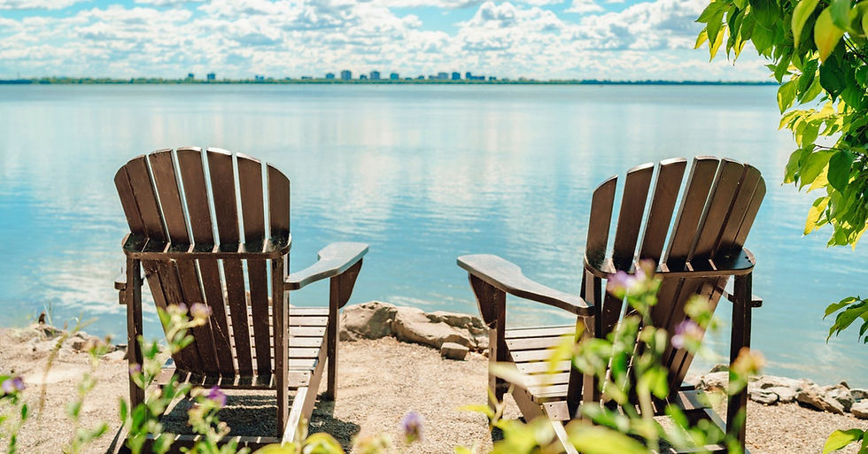 Two Muskoka chairs on a terrace by a calm lake, with a peaceful waterfront view in a cottage-style setting.