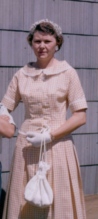 Mother stands proudly in a handmade, well-fitted dress, showcasing her creativity and sewing skills. Her outfit, accessorized with gloves and a matching bag, reflects a timeless elegance.