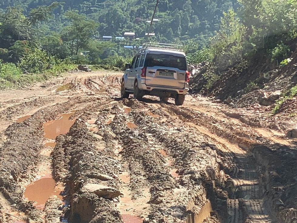 泥だらけの山道を走る白いSUV。深い轍と水たまりが続き、周囲は緑の森に囲まれている。