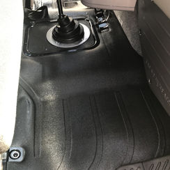 Cleaning rubber floor mats inside semi-truck cab.