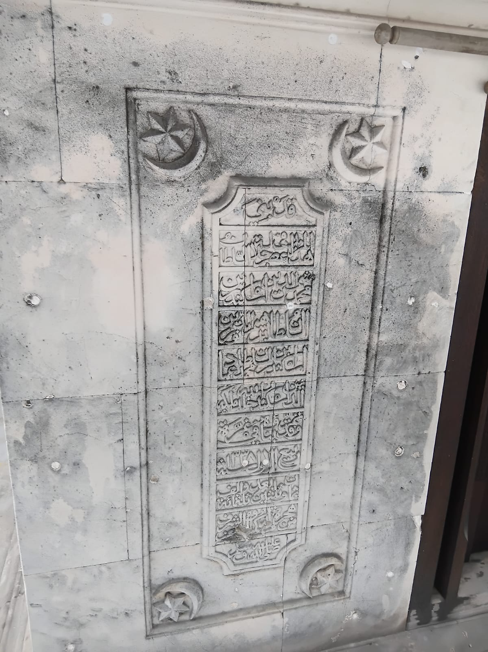 Intricate engravings on the coral wall of Mohamed Thakurufaanu's shrine, featuring Arabic script framed by crescent and star motifs.
